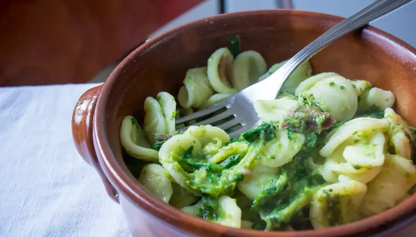 Orecchiette con cime di rapa, uno dei piatti tipici foggiani, servite in una ciotola di terracotta con una forchetta.