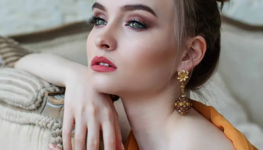Donna con elegante trucco semplice, labbra rosse e orecchini pendenti dorati.
