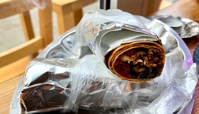 Dwa zawinięte w folię aluminiową i folię spożywczą tureckie wrapy z mięsem i warzywami na talerzu.
