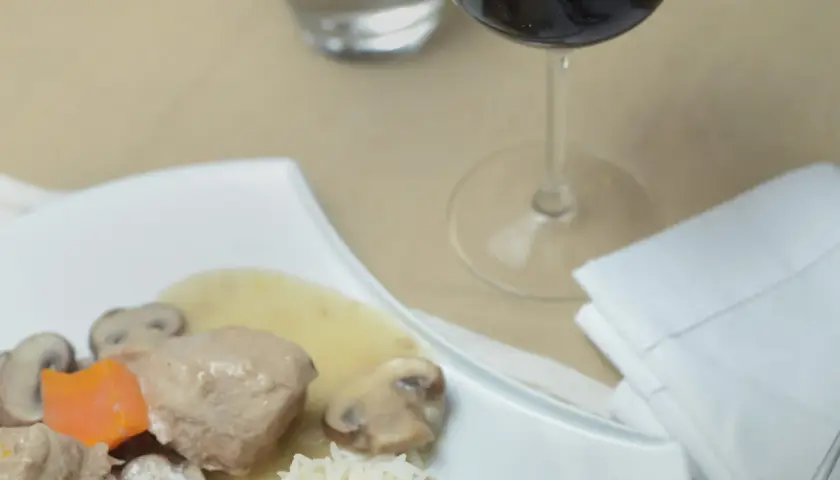 Un verre de vin rouge accompagne une blanquette de veau savoureuse avec riz et champignons.