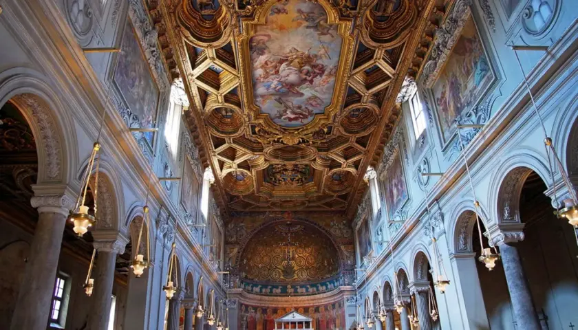Intérieur de la basilique San Clemente à Rome, avec son plafond doré orné de fresques et ses arcs majestueux.