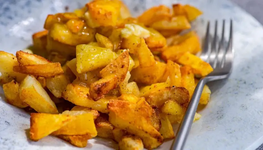 Un plato de papas al horno crujientes, doradas y sazonadas, listas para disfrutar con un tenedor.
