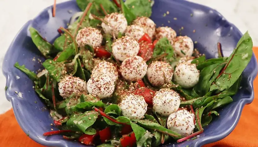 En blå skål med en sallad av gröna blad, körsbärstomater och små, kryddade labneh bollar.