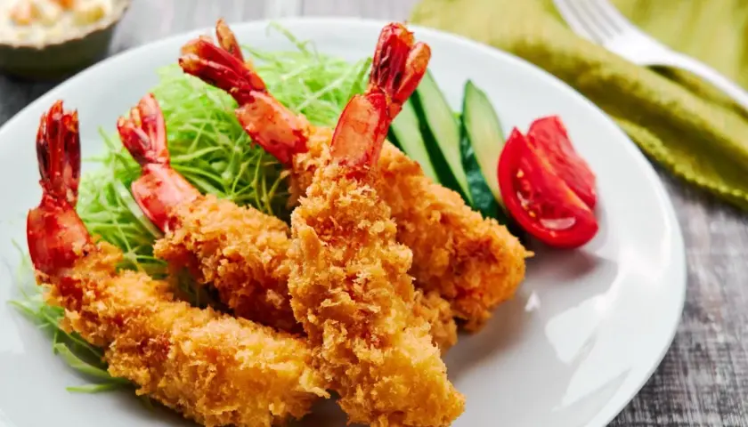 Crispy, golden japanese fried shrimp served on a bed of shredded cabbage with cucumber and tomato slices.