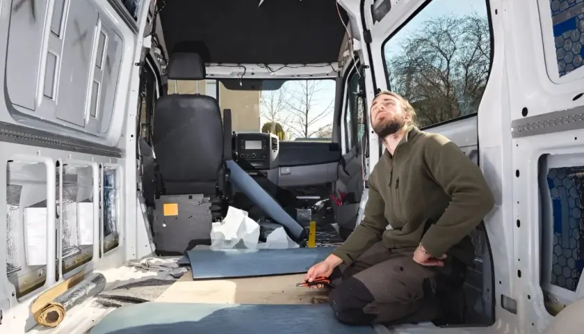 Uomo lavora all'isolamento di un'auto camperizzata. Materiali sparsi, sedili rimossi, pronto per la trasformazione.