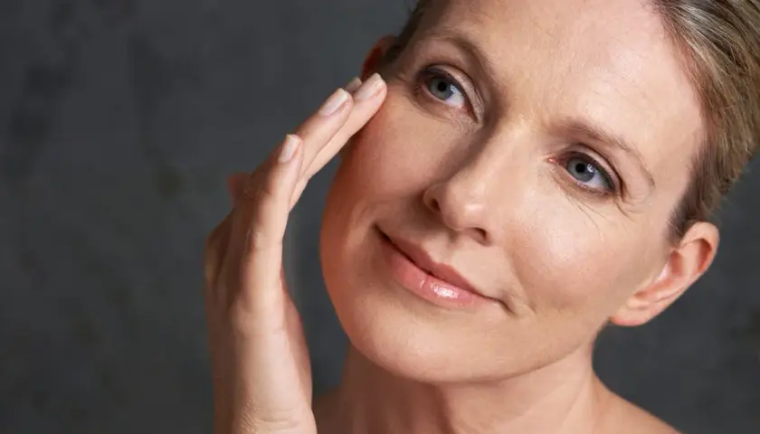 Une femme touche délicatement son visage, révélant une peau mature. La question "peau mature à partir de quel âge" se pose naturellement.