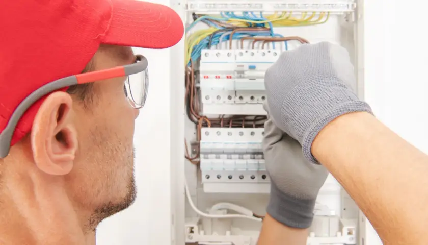 Elektryk w czerwonej czapce i rękawicach pracuje przy skrzynce z przewodami.