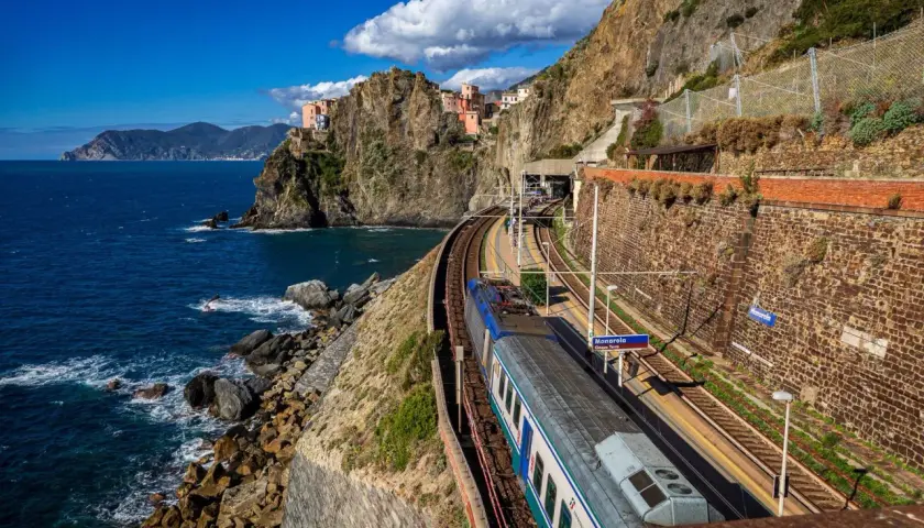 Zug fährt entlang der Küste von Cinque Terre. Bunte Häuser kleben an steilen Felsen über dem blauen Meer.