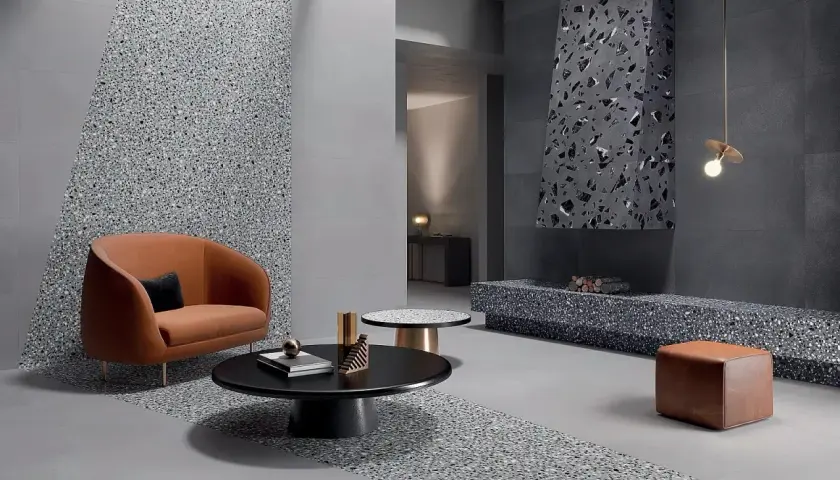 Nowoczesny salon z pomarańczową kanapą i stolikami kawowymi, gdzie dominują szare ściany i podłogi z efektem terazzo. Kominek również ozdobiony terazzo.