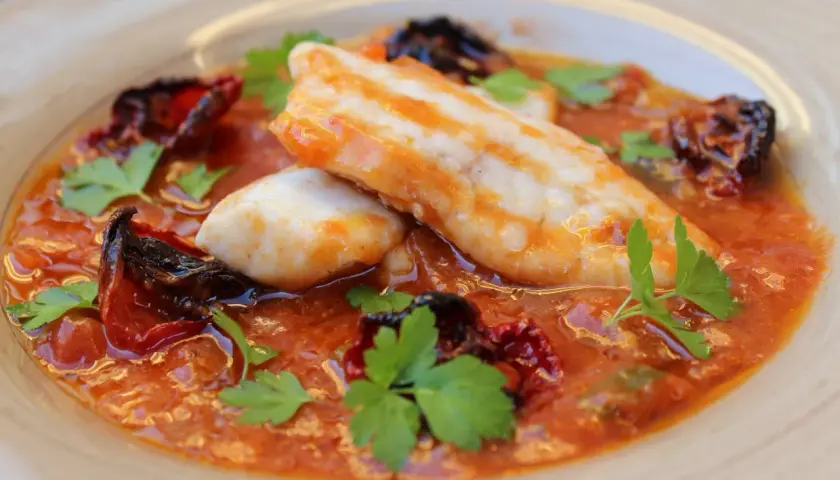 Deliciosa ventresca de merluza en salsa de tomate con pimientos secos y perejil fresco.