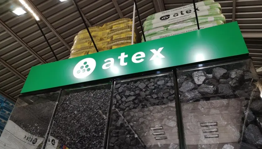 Atex Pilchowice: ceny węgla. Różne rodzaje węgla w gablotach, nad nimi logo Atex i paczki z ekogroszkiem.