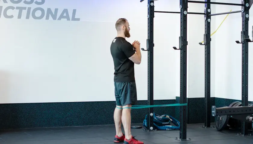 Mężczyzna wykonuje ćwiczenie spanish squat z gumą oporową wokół ud, przygotowując się do przysiadu.