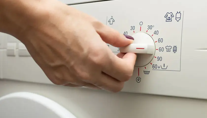 Main d'une personne réglant le bouton d'une machine à laver pour le lavage de vêtements.