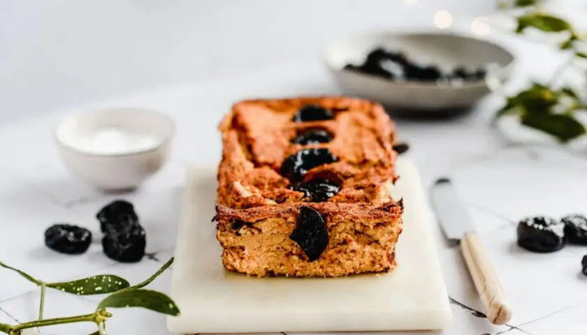 Domowy pasztet z resztek mięsa pieczonego, ozdobiony śliwkami, na desce z nożem i miseczką sosu.