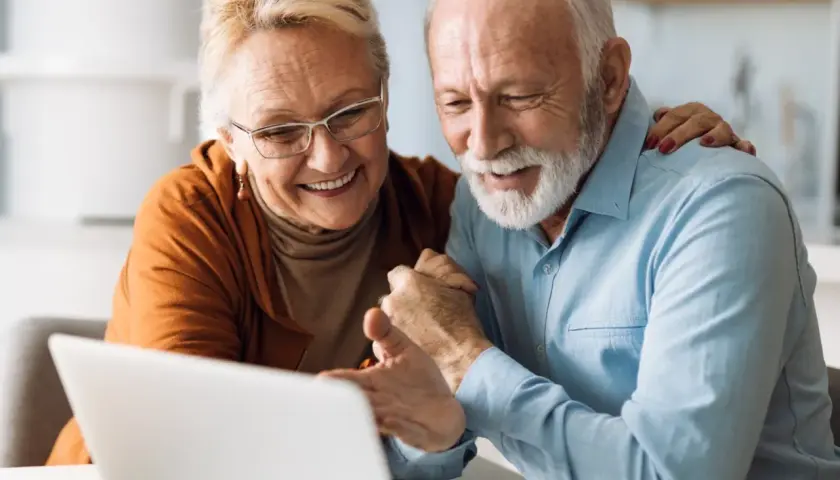 Uśmiechnięta para seniorów korzystająca z laptopa.