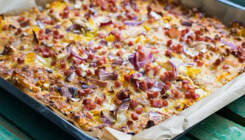 Herzhafte pizza ohne kohlenhydrate mit Speck und roten Zwiebeln, frisch aus dem Ofen auf Backpapier.