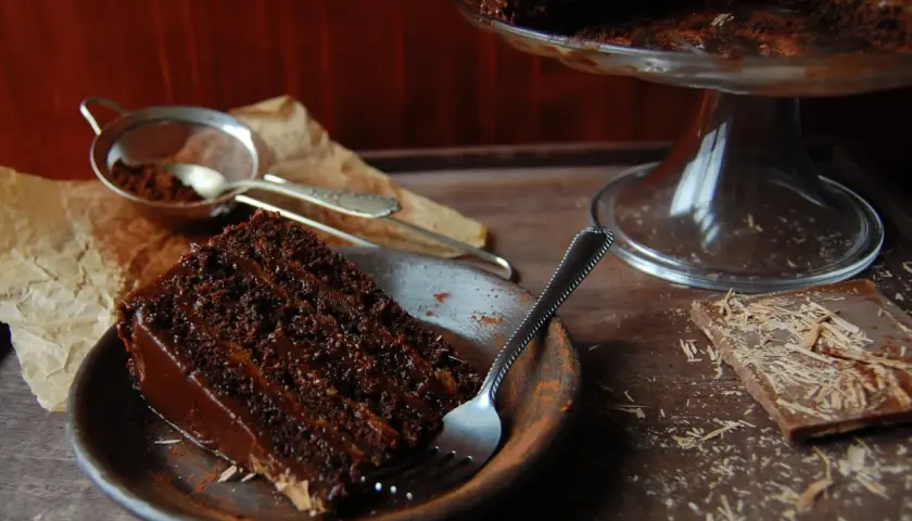 Wilgotny tort czekoladowy z kremem nutella, posypany kakao, czeka na widelca. Obok kawałek czekolady.
