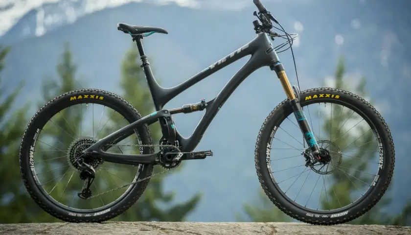 A black Yeti SB5 Turq mountain bike with teal accents sits on a rock, ready for adventure in the mountains.