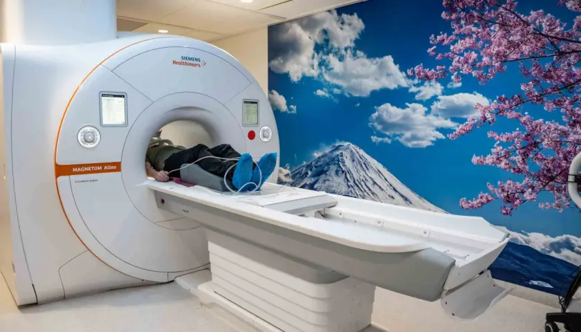 Pacjent leży na łóżku aparatu do rezonansu magnetycznego, przygotowany do badania. W tle widok na górę Fudżi i kwitnące wiśnie.