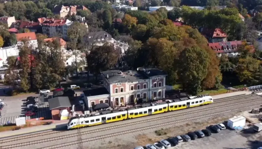 Nowoczesny szynobus pokonuje trasę Wrocław - Trzebnica, mijając malowniczą stację i jesienne drzewa.