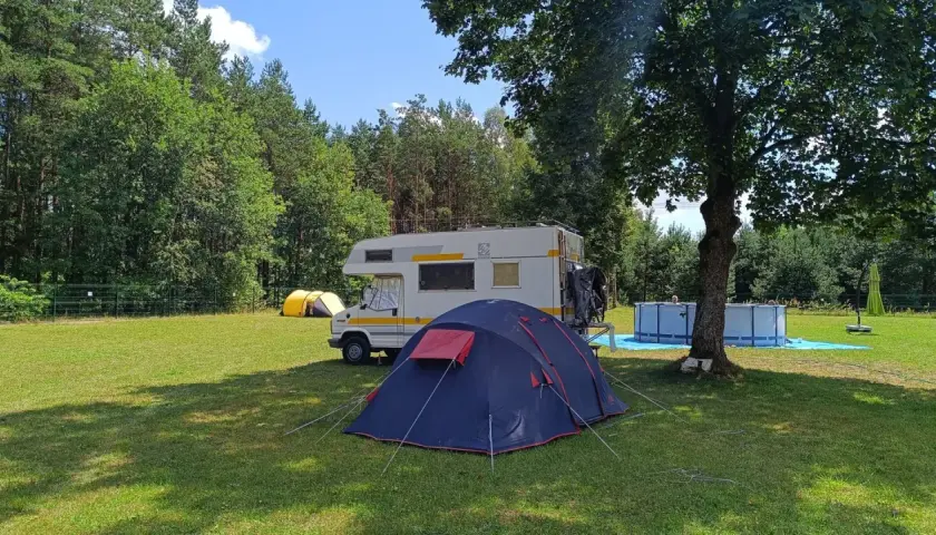 Namiot i kamper na trawie, w tle las i basen. Idealne miejsce na **camping Świętokrzyskie**.