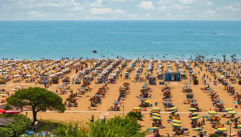 Una spiaggia affollata vicino a Venezia, con file ordinate di ombrelloni gialli e bianchi e persone che si godono il sole e il mare azzurro.
