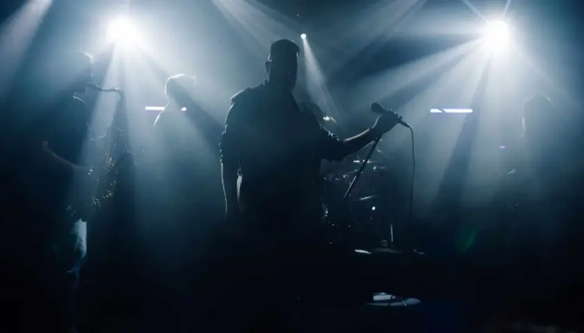 Zespół na scenie, wokalista z mikrofonem, saksofonista. Czy bilety imienne na koncert sprawdzają?