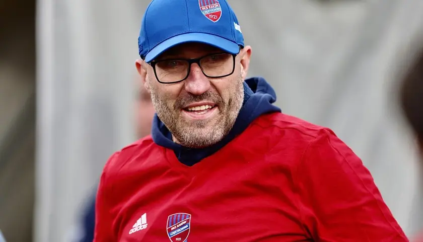 Mężczyzna w niebieskiej czapce i czerwonej koszulce z logo Rakowa Częstochowa.
