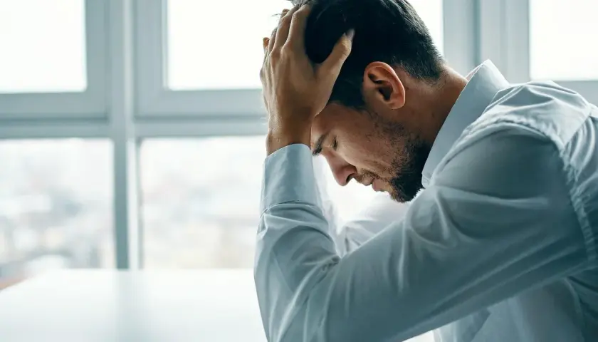 Mężczyzna w białej koszuli z rękami na głowie, pogrążony w myślach, przeżywa kryzys wieku średniego.