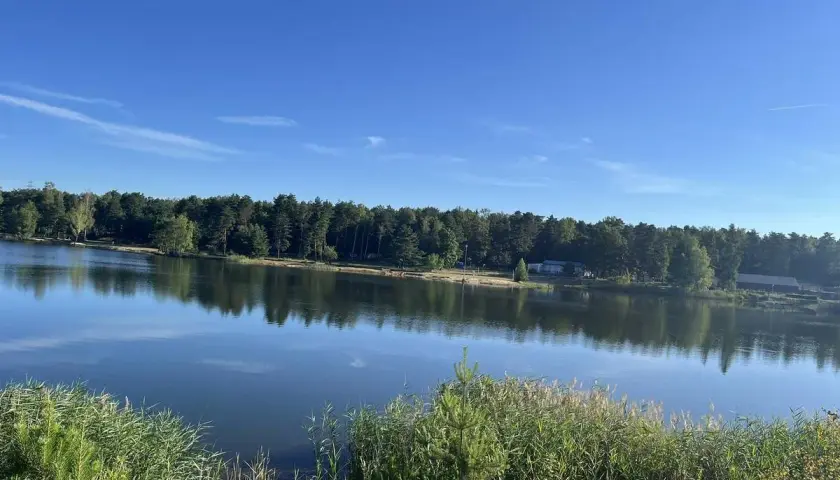 Spokojne jezioro odbija las i błękitne niebo. Trasa nad jeziorem Chechło Nakło zaprasza na spacer.