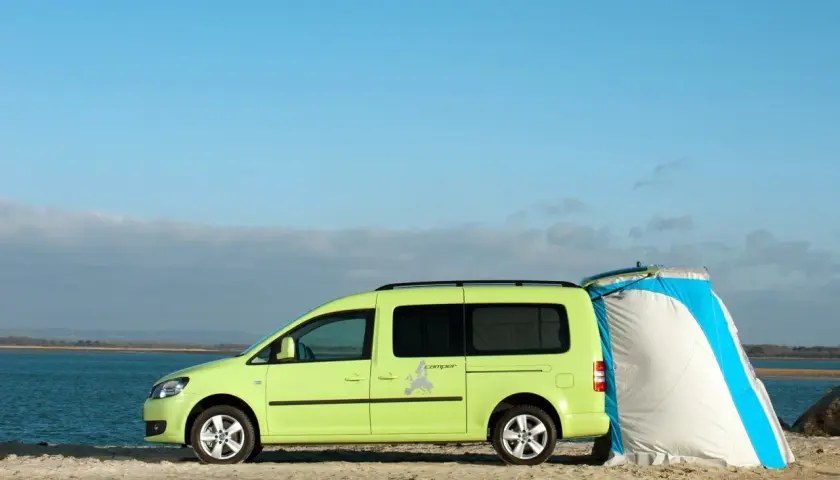 Un caddy tramper vert vif est garé sur une plage, avec une tente bleue et blanche attachée à l'arrière.