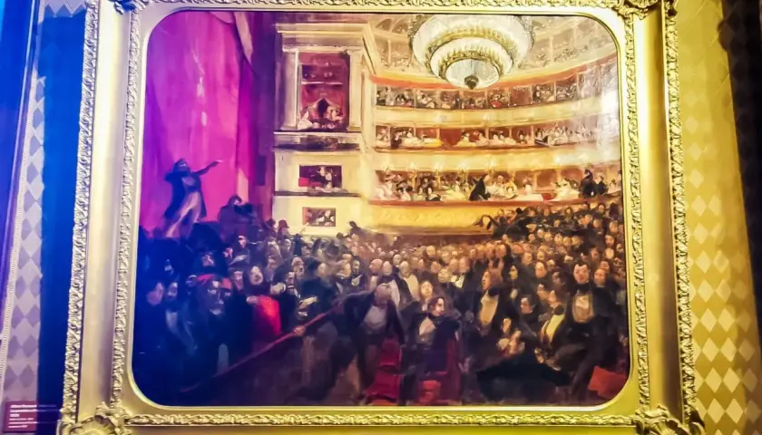 Obraz przedstawia tłum w teatrze, być może inspirowany **najważniejszymi dziełami Victora Hugo**, z widownią i lożami.