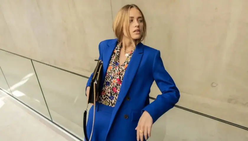 Une femme porte un tailleur-pantalon bleu vif avec une chemise à motifs colorés. Une belle idée tenue travail femme pour un look audacieux.