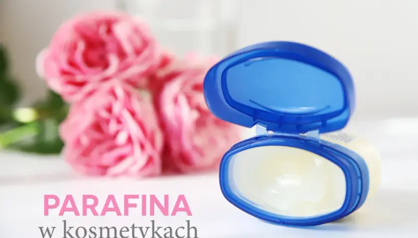 Otwarty słoiczek z wazeliną, która zawiera parafinum liquidum, na tle różowych róż.