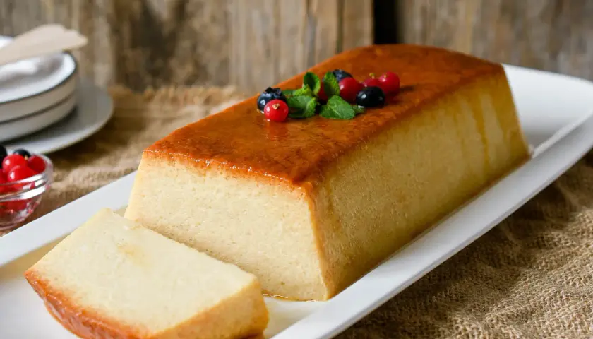 Un delicioso pudin de pan, con una capa dorada y decorado con frutos rojos y menta.