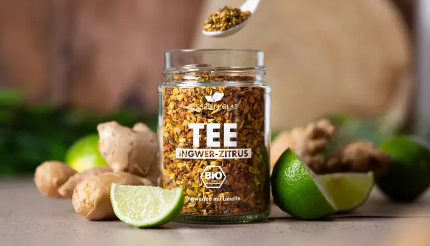Glas mit Ingwer-Zitrus-Tee, frischem Ingwer und Limetten. Perfekt für einen wärmenden Tee, der lange ziehen kann.