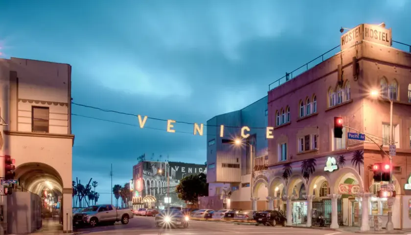 Nocny widok na Venice Beach z neonowym napisem "VENICE" i budynkami hosteli.