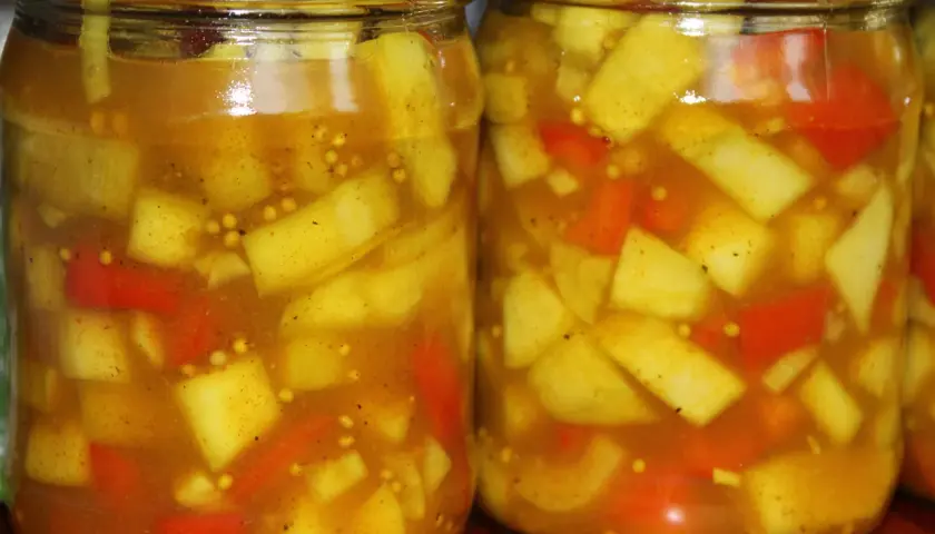 Dwa słoiki z marynowaną cukinią w zalewie curry z kawałkami papryki i gorczycą.