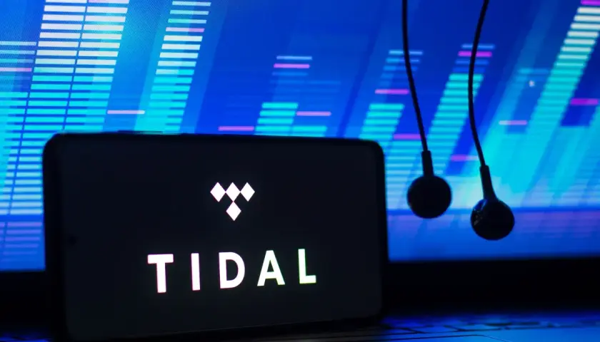 Smartfon z logo TIDAL i słuchawkami na tle wykresu dźwiękowego.
