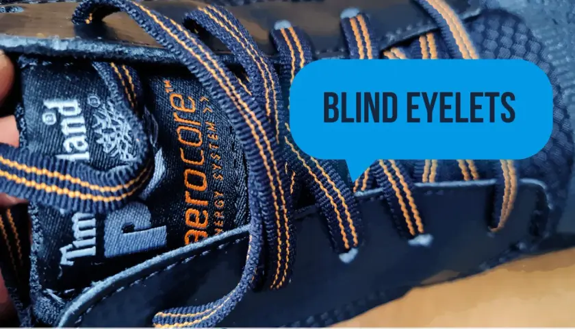 Close-up of a dark blue Timberland boot with orange stitching. The laces go through what are called blind eyelets, a feature that keeps them secure.