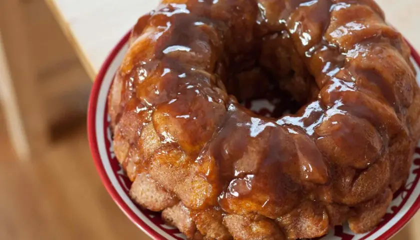 Delizioso monkey bread dorato, ricoperto di glassa lucida, servito su un piatto con bordo rosso.