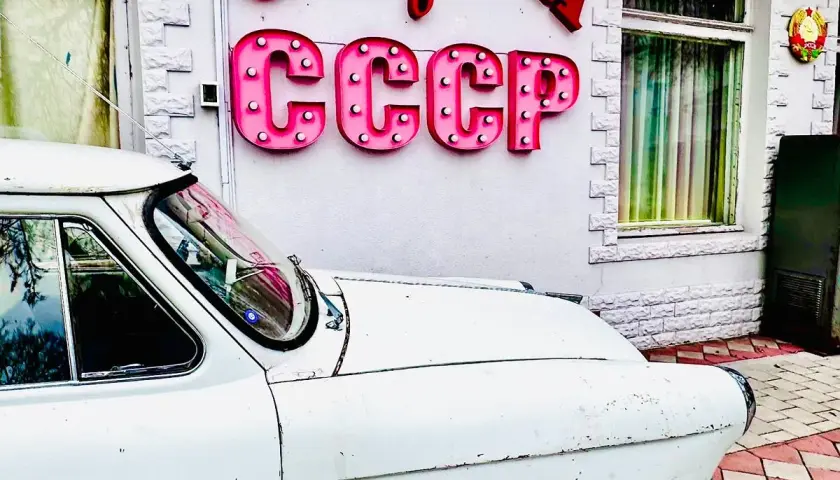 Biały, stary samochód przed budynkiem z neonem CCCP. Czy to podróż w czasie do tamtych lat?