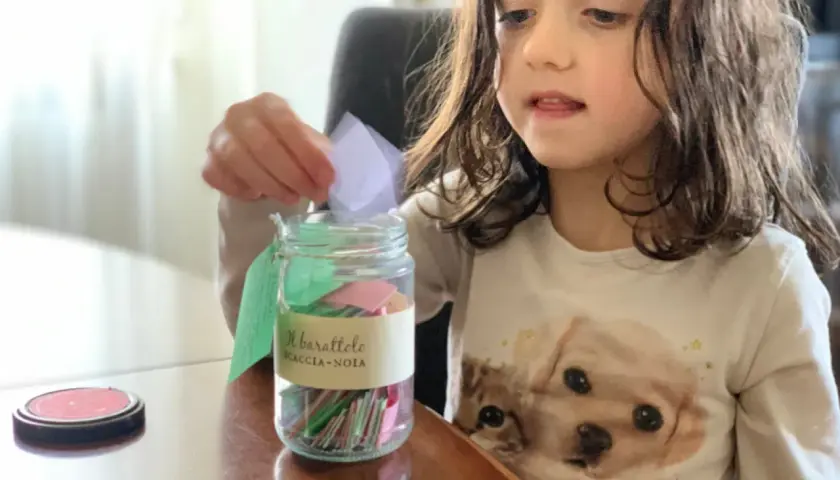 Bambina inserisce un bigliettino nel barattolo "Scaccia-Noia", pieno di idee per giochi da fare quando ci si annoia.