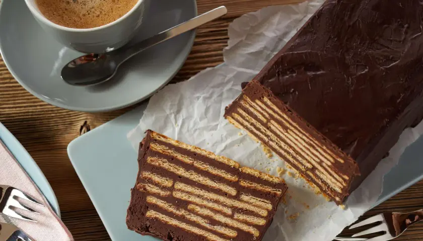 Schokoladiger kalter Hund, geschichtet mit Keksen, neben einer Tasse Kaffee.