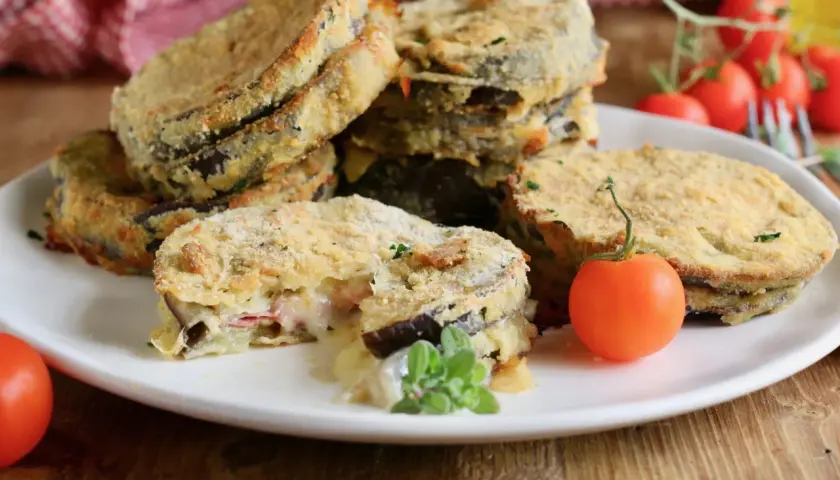 Deliziosi cordon bleu di melanzane impanati e fritti, con un ripieno filante di formaggio e prosciutto, guarniti con pomodorini freschi.