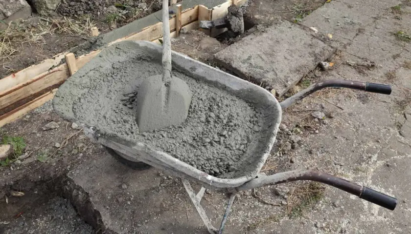 Taczka z betonem i łopatą, gotowa do wylania ławy fundamentowej. Wymiary ławy fundamentowej są kluczowe dla stabilności konstrukcji.