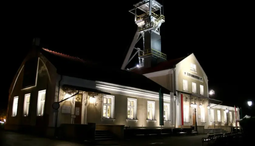 Wieczorem przy szybie kopalni Wieliczka, gdzie można kupić bilety, widać oświetlone budynki i wieżę wyciągową.
