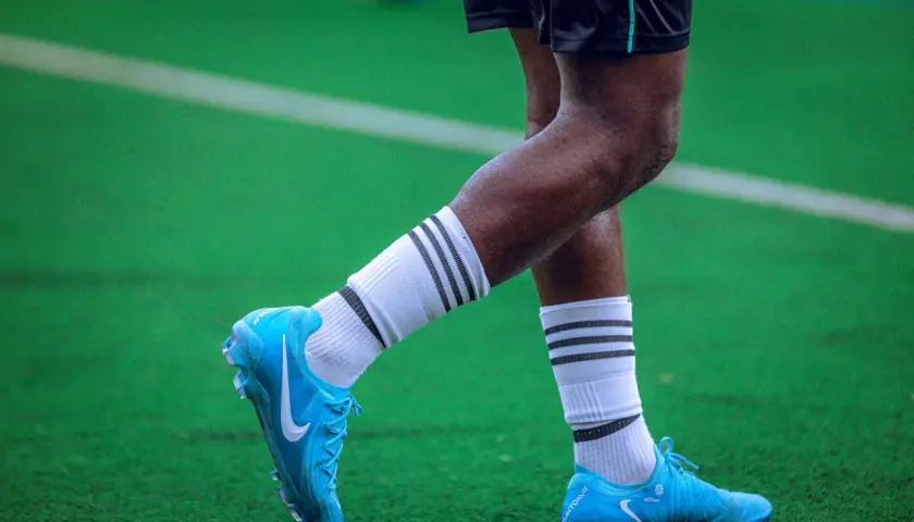 Piłkarz w turfy na zielonej murawie. Jasnoniebieskie buty piłkarskie Nike z białymi skarpetkami i czarnymi paskami.