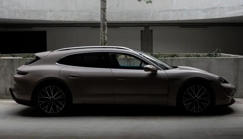 Elegancki Porsche Taycan 4S w kolorze piaskowym, zaparkowany w nowoczesnym garażu z betonowymi ścianami i drzewem.