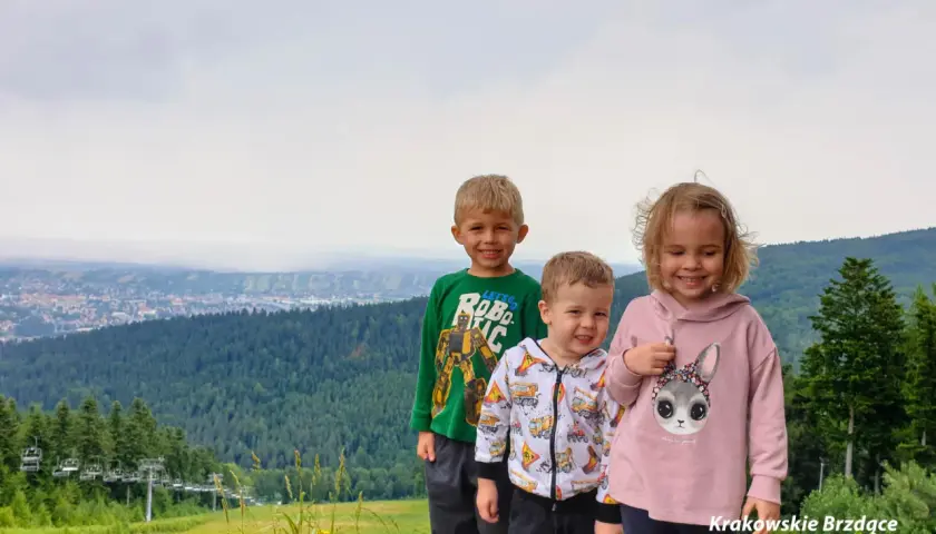 Trójka uśmiechniętych dzieci na tle górskiego krajobrazu z wyciągiem krzesełkowym. Idealne chełm atrakcje dla dzieci na wakacje.